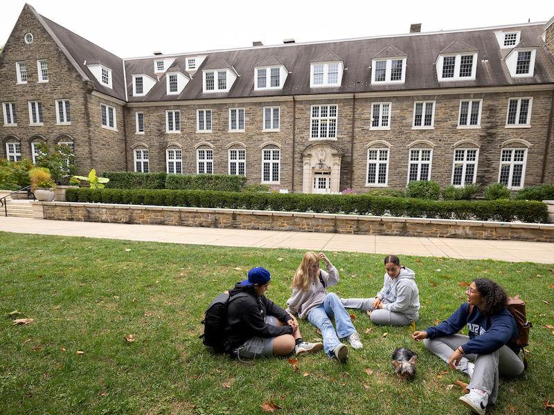 four students sitting on the grass in front of Sutherland building